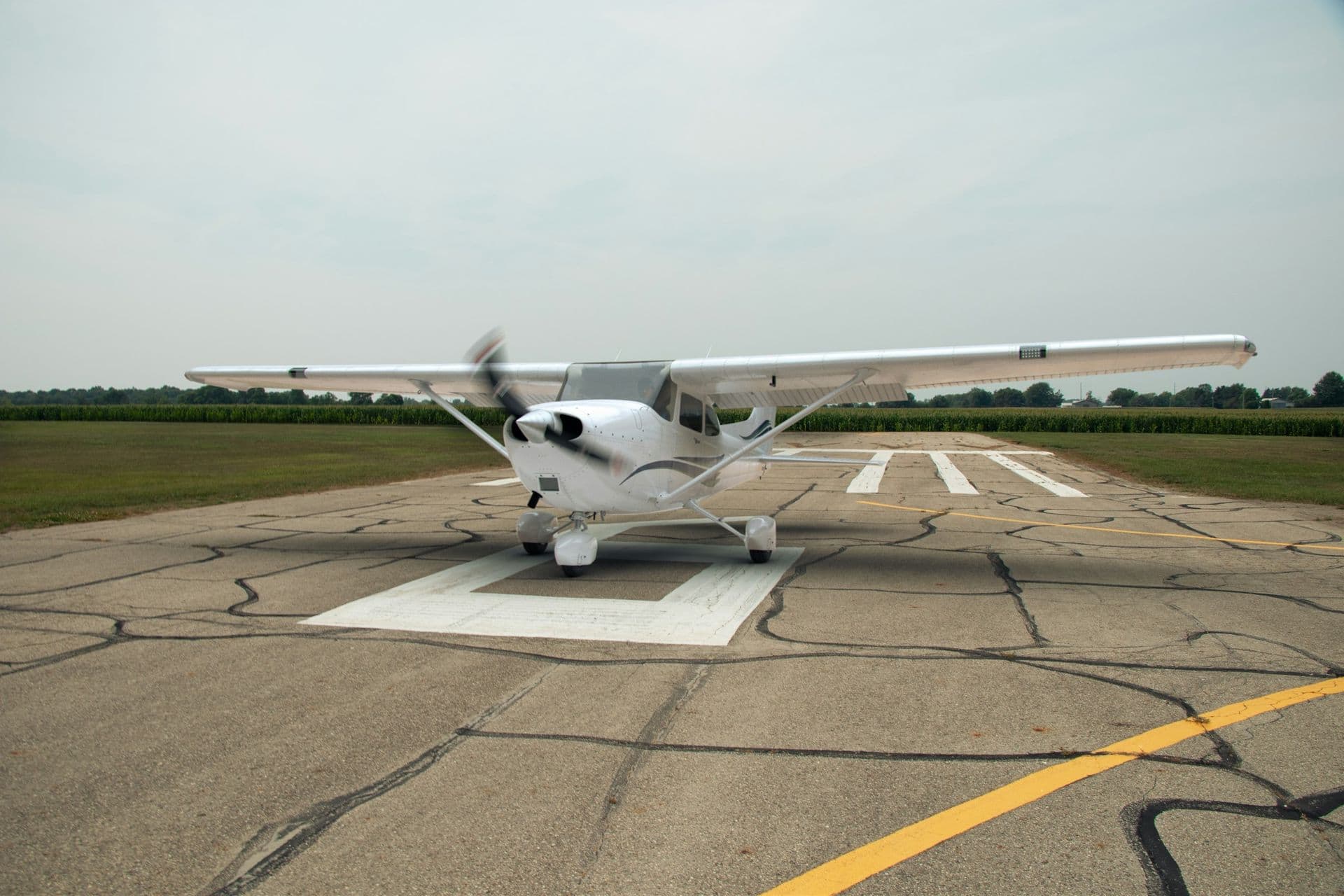 A white Cessna 172 on a runway under an overcast sky, its propeller turning